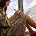 woman sitting with her legs crossed on bed and writing in a journal