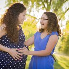 Pregnant mother and daughter (4-5), sitting on bed