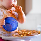 Mother Feeding Baby Sitting In High Chair At Mealtime