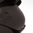 Beautiful pregnant woman holding her back while sitting on a bed