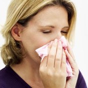 A woman blows her nose with a tissue.