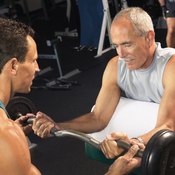 A trainer is helping this older man with preacher curls.