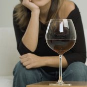 A glass of red wine in front of a woman sitting on a sofa.