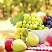 A bowl of red and green grapes on a table with fresh apples and pears