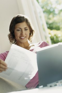 Smiling Woman Sits Behind her laptop Reading a Bill