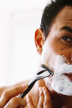 Close-up of a young man shaving his face with a razor