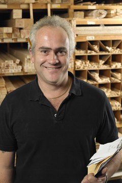 Man holding clip board by planks of wood on shelves, smiling, portrait