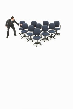 Business man arranging office chairs, forming triangle, studio shot