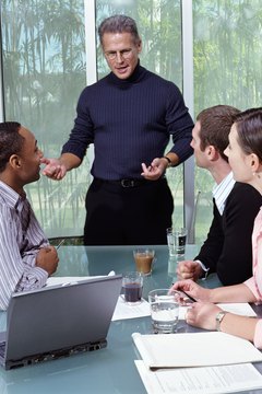 Mature businessman standing by seated colleagues in meeting