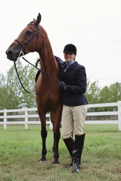 a caucasian female horseback rider stands with her horse and smiles