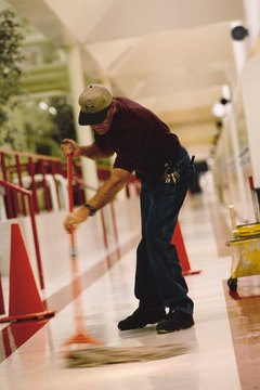 an older caucasian male janitor mops the floor of a hallway