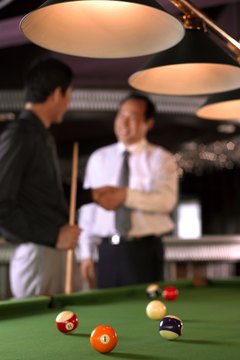 Businessmen shaking hands beside pool table
