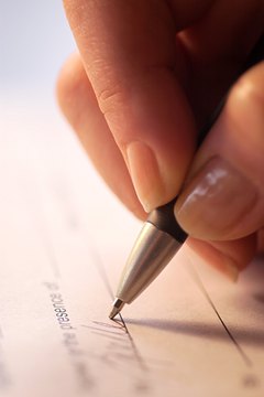 Extreme close-up of woman's hand as she signs her name to a document.