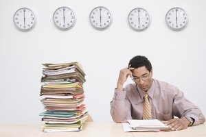 Businessman sitting next to stack of documents on desk, clocks on wall
