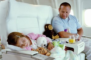 Father looking at daughter (5-7) sleeping on aeroplane