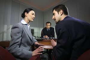 Two co-workers discuss something in front of their boss in a meeting.