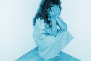 black and white view of a young girl (6-7) sitting in a corner covering her face with her hands