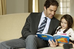 Father reading to daughter (2-4) on sofa, smiling