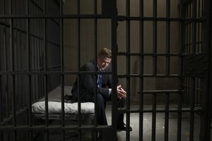 Mature businessman sitting on bed in prison cell