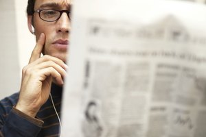 Man reading newspaper, listening to earphones, hand to face, close-up