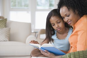 Side profile of a mid adult woman reading a book with her daughter and smiling