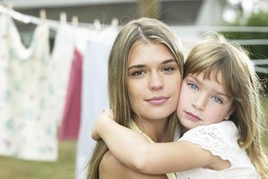 Mother and daughter (4-5) hugging in front of laundry line, portrait