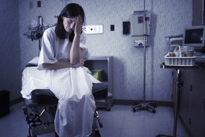 a concerned caucasian female patient dressed in a hospital gown sits in an exam room and looks worried