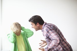 Boy covering ears as mature man shouts at him