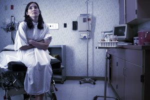 a caucasian female patient in a hospital gown sits in an exam room and waits