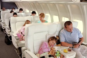 Girl (5-7) asleep on plane surrounded by soft toys, next to father
