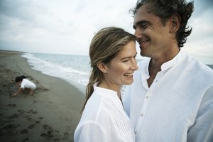 Couple on beach, children (7-9) playing in background