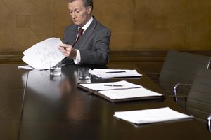 Mature man reading papers at end of table in conference room