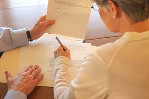 Close-up rear view of a woman signing legal documents at a table.