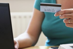 Woman using laptop computer, holding credit card, close-up