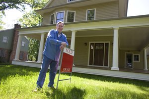 Man standing with for sale sign in front of home