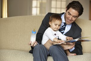 Father reading to daughter (15-18 months) on sofa, smiling