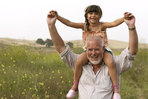 Girl (4-6) sitting on grandfather's shoulders, smiling, portrait