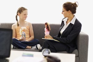 female psychiatrist sitting with a girl on a sofa playing with dolls