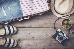 Travel preparations concept with suitcase, clothes and accessories on an old wooden table.