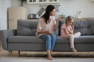 Mom scolds little daughter sitting on couch