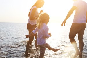 Happy young family having fun running on beach at sunset