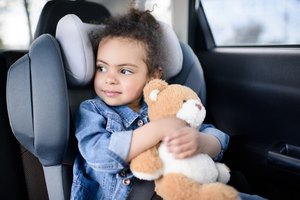 little girl holding teddy bear while sitting in car