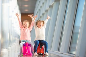 Adorable little girls having fun in airport sitting on suitcase