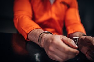 Male prisoner in orange jumpsuit wearing handcuffs