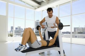 A woman gets spotted while bench pressing.