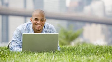 Doctorate student typing on laptop while laying in the grass.
