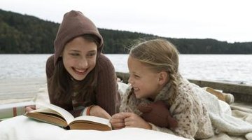 Children reading a book on a lakeside.