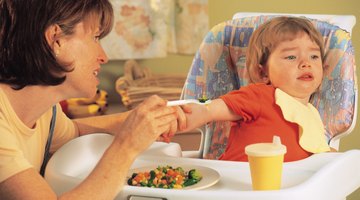 Baby girl (18-24 months) in high chair, spaghetti hanging over tray