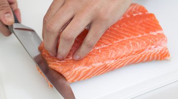 person using a fork and knife on a plate of grilled salmon