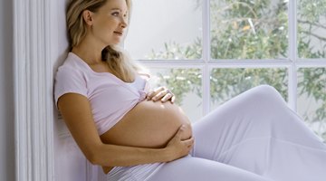 Pregnant woman with cramping and lower back pain sitting on her bed